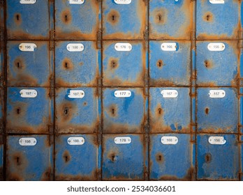 Close up on four rows of abandoned unused rusted blue painted mailboxes with numbering still on them.  