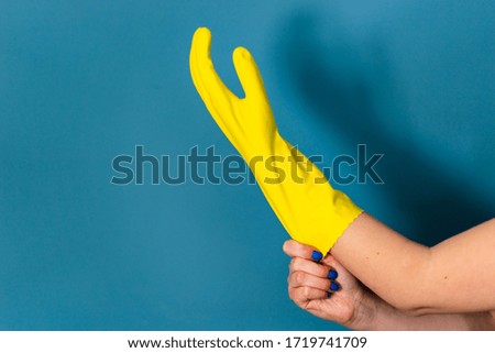 Close up on hand of unknown caucasian woman female girl putting on adjusting holding protective yellow rubber gloves to clean or disinfection against blue wall background in day
