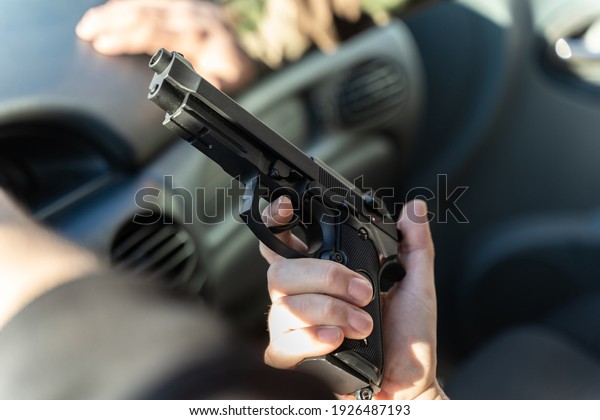 Close up on hand of unknown caucasian man holding a\
gun in car