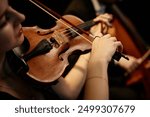 Close up on hand of unrecognizable female orchestra musician playing violin with bow during concert on stage, focus on hand and tailpiece