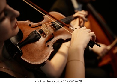 Close up on hand of unrecognizable female orchestra musician playing violin with bow during concert on stage, focus on hand and tailpiece