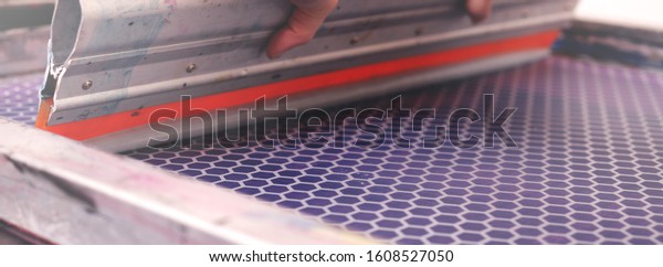 Close up on a hand-guided\
screen printing squeegee shoving silver paint over a silk-screen\
frame - handicraft and exclusive fashion concept - background\
blanked out blurry