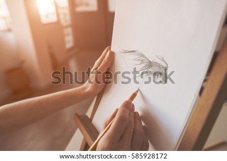 close up on the hands of an artist drawing a pencil sketch of a fish