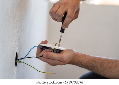Close up on hands of caucasian man electrician holding screwdriver working on the plug electric on residential electric system installing white AC power socket on gray wall at home repair close up - Shutterstock ID 1739732096