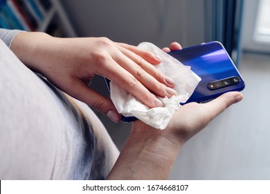 Close Up On Hands Of Caucasian Young Woman Female Holding Mobile Smart Phone In Hand Wiping Cleaning Screen Disinfection With White Wet Wipe Towel Napkin Alcohol Anti Virus And Bacteria Prevention