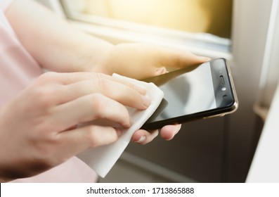 Close Up On Hands Of Caucasian Young Woman . Female Holding Mobile Smart Phone In Hand Wiping Cleaning Screen Disinfection With White Wet Wipe Towel Napkin. Alcohol Anti Virus And Bacteria Prevention