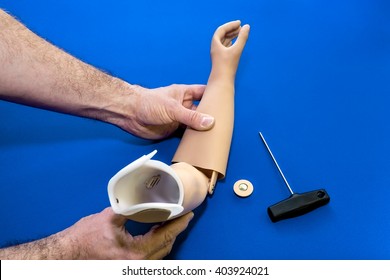 Close Up On Hands And Tools Adjusting Prosthetic Arm Elbow Joint In Light Skin Tone Color Over Isolated Blue Background