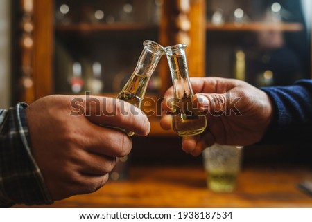 Close up on hands of two unknown men toasting with traditional serbian drink plum brandy rakija slivovitza holding glass called cokance at home