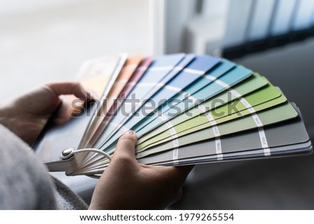 Close up on hands of unknown female person holding color palette at home in apartment - Woman choosing paint material for house renovation - decoration and innovation concept