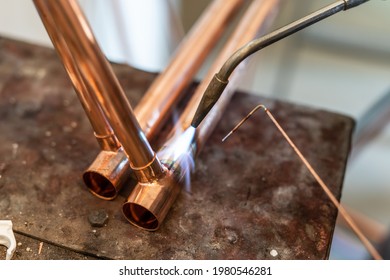 Close up on hands of unknown industrial worker plumber with central heating copper pipes welding using gas torch or blowtorch at work
