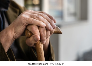 Close up on hands of unknown old caucasian man pensioner senior holding cane walking stick while sitting and waiting - real people old age senility concept copy space