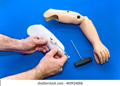 Close Up On Hands Using Tools To Assemble Prosthetic Arm In Light Skin Tone Color Over Isolated Blue Background