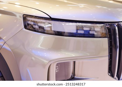 Close up on headlight of modern SUV automobile. White demo vehicle with pearlescent shine displayed in car showroom at dealership center
