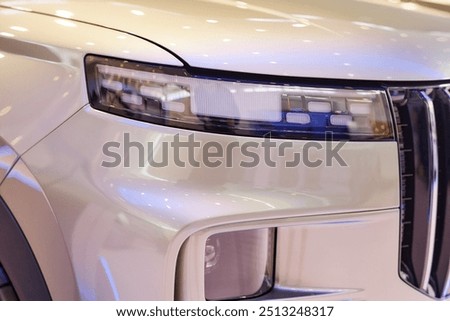 Close up on headlight of modern SUV automobile. White demo vehicle with pearlescent shine displayed in car showroom at dealership center
