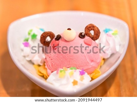 Close up on a Japanese strawberry ice cream and cheerios shaped as a cute bear character topped with sweet whipped cream and colorful sugar decorations on corn flakes.
