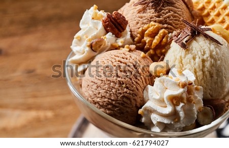 Close up on large ice cream dessert with chocolate, vanilla, waffle cone and nuts on top