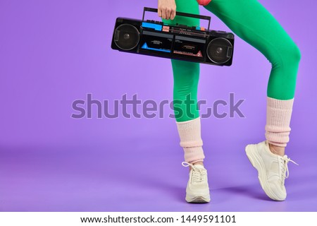 close up on legs and portable radio cassette player, cropped shot of unrecognizable athletic sporty woman standing in green leggins and white training shoes