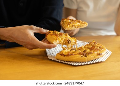 close up on man hand hold piece of sliced chicken BBQ pizza on the plate and sharing with friend on the table in restaurant for leisure and relax lifestyle on weekend concept