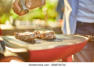 Close Up On Man's Hand Seasoning Meat On The Gas Grill On Barbecue Grill Outdoor In The Backyard, Grilled Roasted Steak Meat, Summer Family Picnic, Food On The Nature.