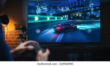 Close Up on Man's Hands at Home, Sitting on a Couch in Stylish Loft Apartment and Playing Arcade Car Video Games on Console. Male Using Controller to Play Street Racing Drift Simulator. - Shutterstock ID 2149430985