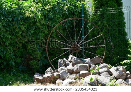 A close up on a metal wheel being a part of an old cart located next to a bunch of rocks, stones, or boulders next to some shrubbery spotted on a sunny summer day on a Polish countryside