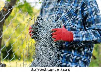Close up on midsection of unknown man holding protective chain link diamond wire fence in the field in day with copy space - Shutterstock ID 1854661549