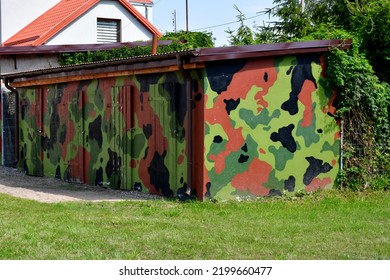 Close up on a military shed, shelter, or shack painted in camo colors and overgrown with vines and other plants seen in the middle of a public park next to a well maintained lawn on a sunny summer day