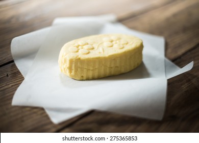 Close Up On A Mound Of Rustic Butter Wrapped In Paper Placed On A Wooden Table