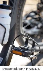 Close Up On A Mountain Bike Pedal With Strap Style Toe Clip, With Bicycle Frame In The Blurry Background And Space For Text On Top