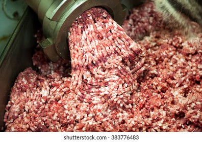 Close up on the nozzle of an industrial mincing machine with fatty mince meat extruding into a container below in a butchery during preparation of meat products