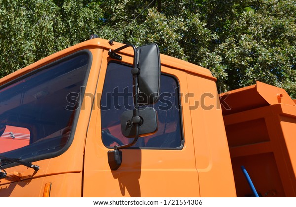 A close up on an orange dump\
truck, garbage truck cabin with rear view, side view\
mirrors.