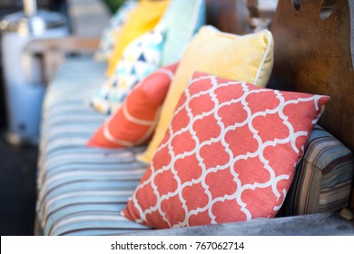 Close up on orange and yellow pattern throw pillows on an outdoor patio chair, with a blue striped cushioned bench 
