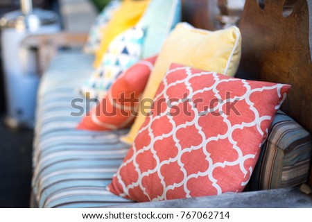 Close up on orange and yellow pattern throw pillows on an outdoor patio chair, with a blue striped cushioned bench 