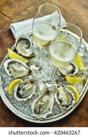 Close up on oysters set up around silver platter filled with crushed ice, lemon slices and champagne glasses in middle