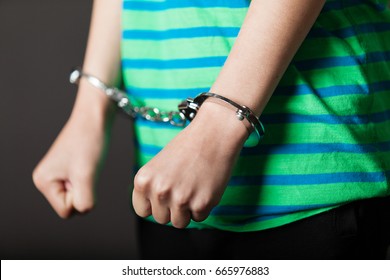 Close up on pair of hands from child or teenager in green and blue shirt tied with metal handcuffs - Shutterstock ID 665976883