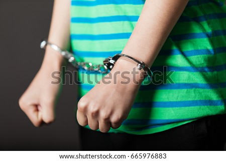 Close up on pair of hands from child or teenager in green and blue shirt tied with metal handcuffs