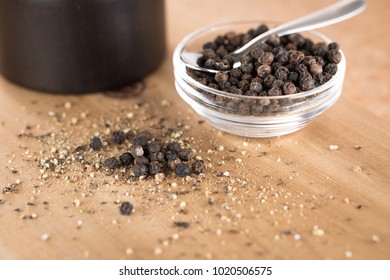 Close Up On A Pile Of Freshly Cracked Black Pepper On A Wood Cutting Board, Beside A Glass Dish Of Whole Peppercorns, And A Grinder In The Background