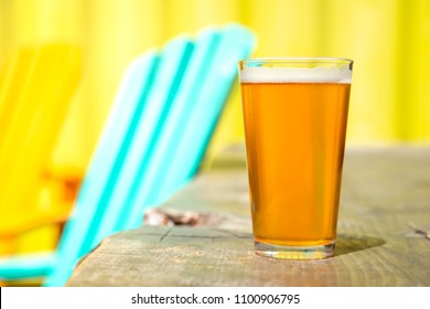 Close Up On A Pint Of Amber Lager Beer, With Patio Furniture And A Bright Yellow Background, With Space For Text On Left