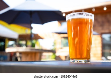 Close Up On A Pint Glass Of Amber Ale Beer, At An Outdoor Patio Of A Craft Brewery, With Space For Text On The Left