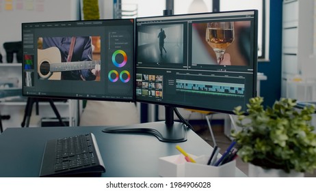 Close up on professional computer placed on desk, dual monitor setup processing video film montage in empty creative workplace. Video editing start up studio company agency with no people in it - Shutterstock ID 1984906028