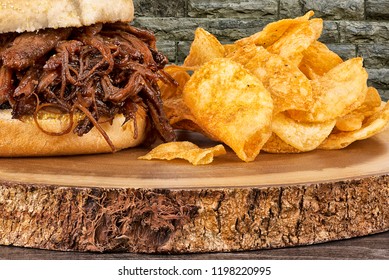 Close up on pulled pork sandwich and potato chips. Wall of bricks in background.