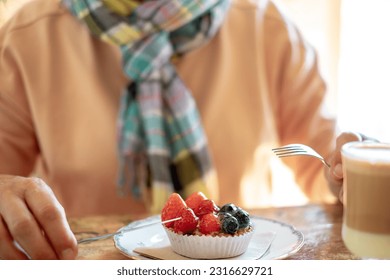 Close up on senior woman ready to eat a fresh fruit cake sitting at cafe table enjoying break or breakfast ignoring diets - Powered by Shutterstock