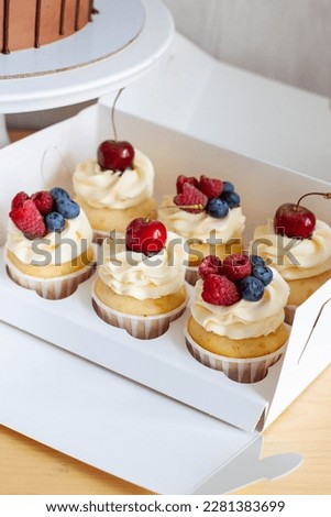 Close up on a set of cupcakes decorated with fresh berries, cherry, strawberry and blueberry on gift box