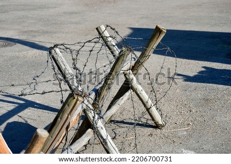 A close up on a small barricade made out of planks, logs, and sticks, with some barbed wire attached to it seen on a concrete floor on a Polish countryside during a military picnic or fair 
