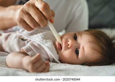 Close up on small caucasian baby four months old and hand of unknown father giving her medicine antibiotics while lying on bed at home parenthood and health issues liquid drugs oral syringe concept
