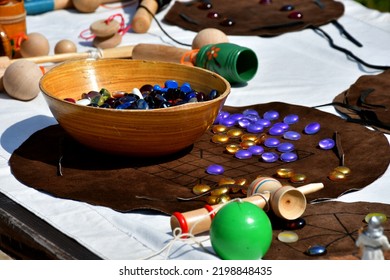 A Close Up On A Table Full Of Medieval Games And Accesories, Such As A Bowl With A Lot Of Colorful, Vivid Marbles, Wooden Toys, Some Chess Set And Other Items Seen On A Sunny Summer Day In Poland