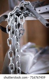 Close Up On Tangled Metal Chain Hanging Off Of A Cluttered Shelf With Pipes, In A Mechanics Shop