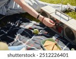 Close up on teenage boys hand turning up volume on vintage boombox as young friends enjoying picnic in nature on sunny day, copy space