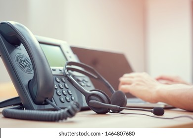 close up on telephone office desk with employee call center man hand typing on a keyboard at desktop pc for working in operation room , communication technology concept