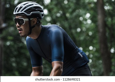 Close Up On Tried Face Of Asian Man, Who's Waring Sunglasses, White Helmet And Blue Cycling Jersey Riding In A Rain.